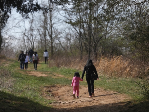 a photo of people hiking on a trail in the distance, with a mom and a little girl wearing pink in the foreground