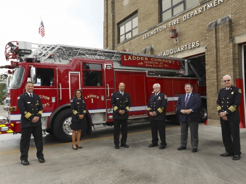 one woman and five men in navy uniforms pose in front of a fire truck