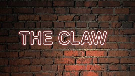 "The Claw" in neon text on a brick background.