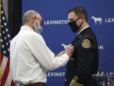 man in formal fire department uniform having a badge placed on his jacket chest by an older man