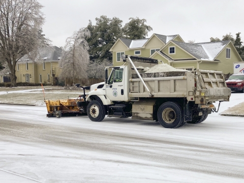 snow/salt truck going down a snow covered street in a residential neighborhood