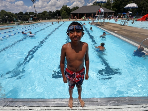 young boy sinding near edge of large, outdoor, inground swimming pool