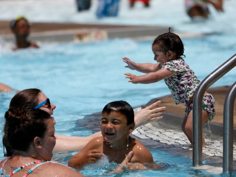 toddler jumping into adults arms at the edge of an outdoor public swimming pool