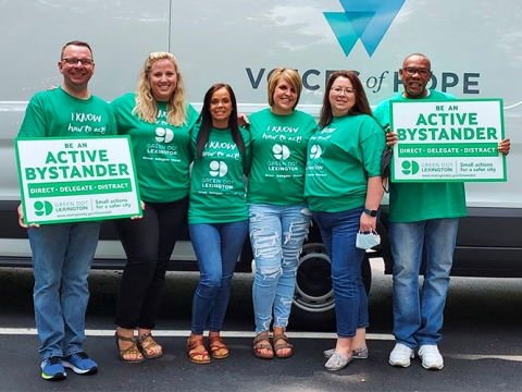 Members from Voices Of Hope-Lexington, Inc. stand together in front of a van wearing and displaying their active bystander gear.