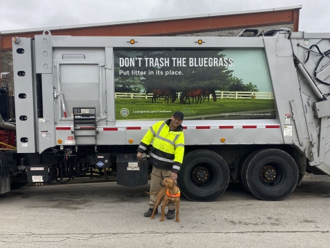 man in safety gear holding dog near garbage truck