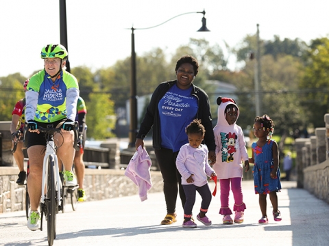 Woman riding a bike and female with three children walking on the Brighton Trail